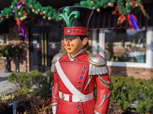 A colorful toy soldier statue in a festive outdoor setting, decorated with holiday greenery and ornaments.