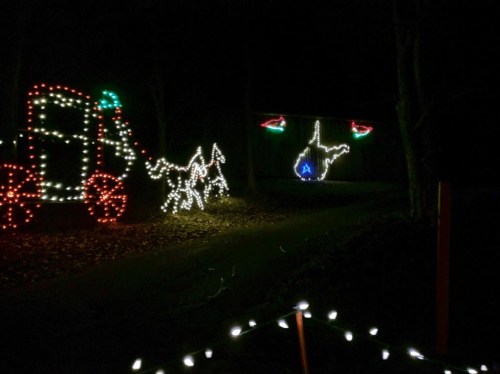 Colorful holiday lights display featuring a tractor, horses, and a map outline of West Virginia against a dark background.