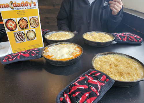 A table with four bowls of macaroni and cheese, a menu, and colorful chili-themed pot holders.