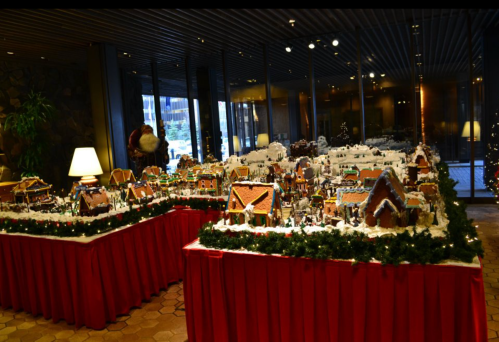 A festive display of gingerbread houses arranged on tables, decorated with snow and greenery, in a warmly lit room.
