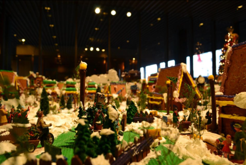 A festive gingerbread village scene with colorful houses, trees, and snowy decorations, illuminated by warm lights.