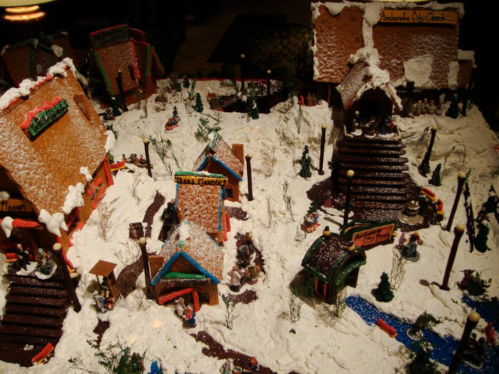 A festive gingerbread village with snowy rooftops, colorful buildings, and miniature figures in a winter scene.