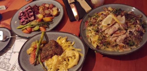 Three plates of gourmet food: grilled chicken pasta, steak with vegetables, and a meatball dish with fettuccine.