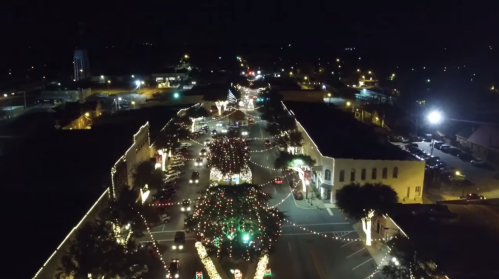 Aerial view of a festive street at night, adorned with colorful holiday lights and decorations.