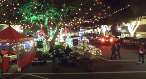 A festive street scene with colorful lights, a live band performing, and people enjoying the holiday atmosphere.