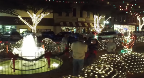 A festive street scene with a fountain, holiday lights, and people enjoying the decorations.
