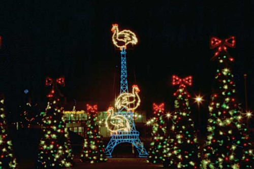 A festive scene featuring a lit Eiffel Tower with turkeys on top, surrounded by Christmas trees and bows.