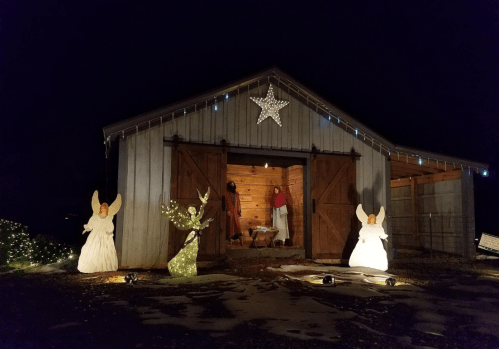 A barn at night decorated with lights and angel figures outside, creating a festive atmosphere.
