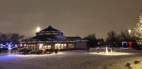 A festive building adorned with colorful lights, surrounded by snow and illuminated trees on a winter night.