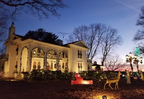 A beautifully decorated house for Christmas, featuring lights, wreaths, and festive ornaments against a twilight sky.