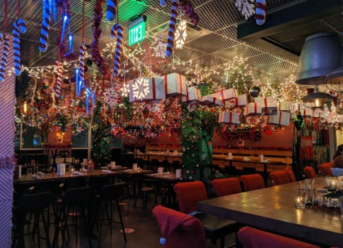 A festive restaurant decorated with colorful lights, hanging gifts, and holiday ornaments, creating a cheerful atmosphere.