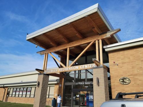 Exterior view of Sprinker Recreation Center, featuring a wooden entrance and signage for ice rink and tennis facilities.