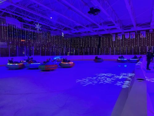 Colorful bumper cars on ice under blue lights and festive decorations, with people enjoying the activity.