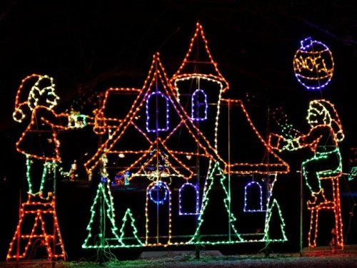 Colorful holiday lights depict two elves decorating a whimsical house with trees and ornaments.