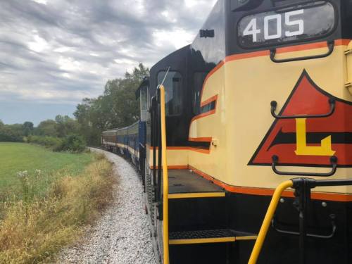 A colorful train engine on a curved track, surrounded by green fields and a cloudy sky.