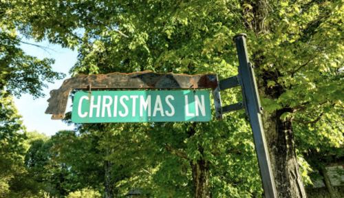 A weathered street sign reading "CHRISTMAS LN" surrounded by green trees.