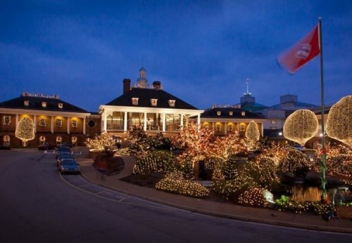 A beautifully lit building at dusk, surrounded by festive lights and decorated trees, with a flag waving in the foreground.