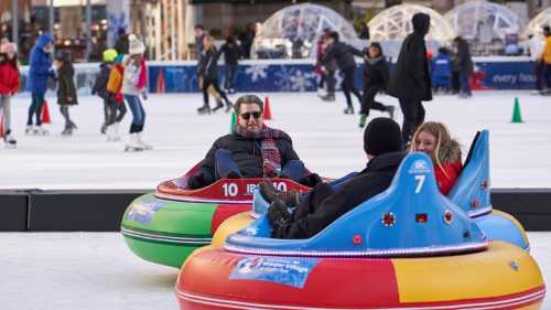 Two people sit in colorful bumper cars on an ice rink, surrounded by skaters and festive decorations.