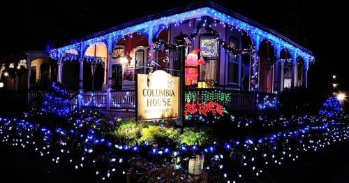A beautifully decorated house with blue and white lights, featuring a sign that reads "Columbia House" and festive decorations.
