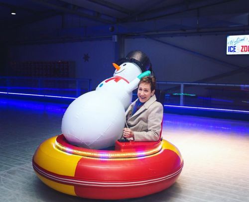 A person smiles while sitting in a colorful inflatable ring with a large snowman on an ice rink.