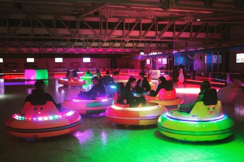 A colorful indoor rink with people in bumper cars, illuminated by vibrant lights in a festive atmosphere.