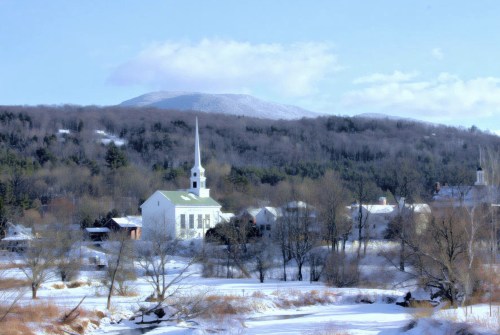 A snowy landscape featuring a white church with a steeple, surrounded by trees and mountains in the background.
