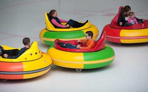 Four colorful bumper cars on an ice rink, with children and adults enjoying a fun ride together.