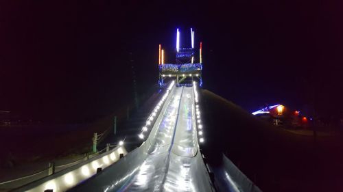 A brightly lit water slide at night, featuring colorful lights and a steep descent.