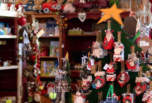 A festive display of Christmas ornaments and decorations in a cozy shop, with a decorated tree and colorful items.