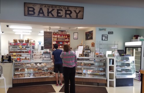 A bakery display with various baked goods, featuring two customers at the counter in a cozy shop setting.