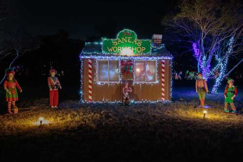 A festive display of Santa's workshop with colorful lights and cheerful elf decorations in a nighttime setting.