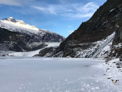 A snowy landscape featuring a frozen lake, mountains, and a waterfall under a clear blue sky.
