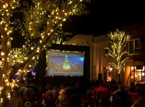 Outdoor movie screening of "The Polar Express" with festive lights and a decorated tree in the background.