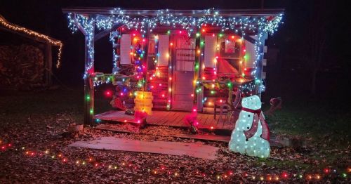 A cozy cabin decorated with colorful Christmas lights and a snowman in front, surrounded by fallen leaves.