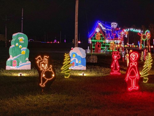 Colorful holiday lights illuminate a festive scene with decorated trees, a house, and cheerful characters in the night.