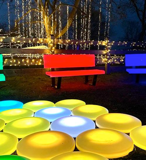 Colorful illuminated benches and circular lights in a festive outdoor setting with twinkling fairy lights.