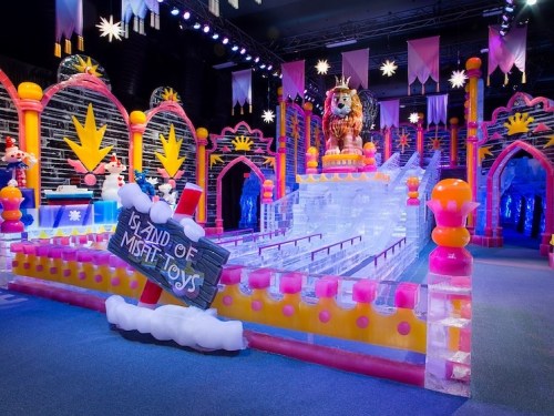 Colorful ice sculpture display featuring a lion, whimsical decorations, and a sign reading "Island of Misfit Toys."
