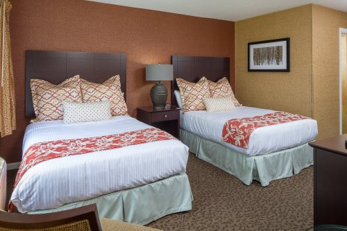 A cozy hotel room featuring two beds with decorative pillows, a lamp, and warm-toned walls.