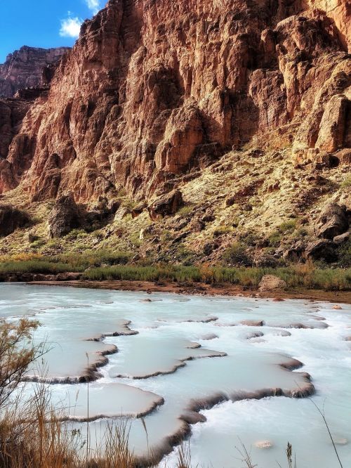 A serene river flows through a rocky canyon, with lush greenery and unique, wavy patterns in the water.
