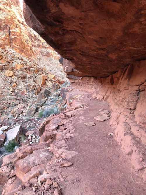 A rocky canyon with a narrow path beneath a large overhanging rock formation.
