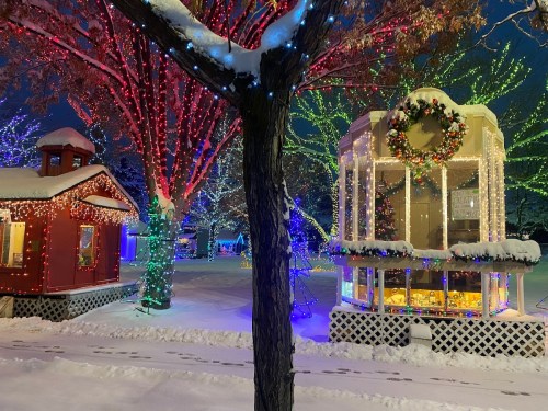 A snowy scene with colorful holiday lights on trees and a decorated gazebo, creating a festive winter atmosphere.