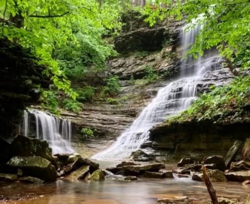 A serene waterfall cascading over rocky cliffs, surrounded by lush green foliage and a calm pool below.