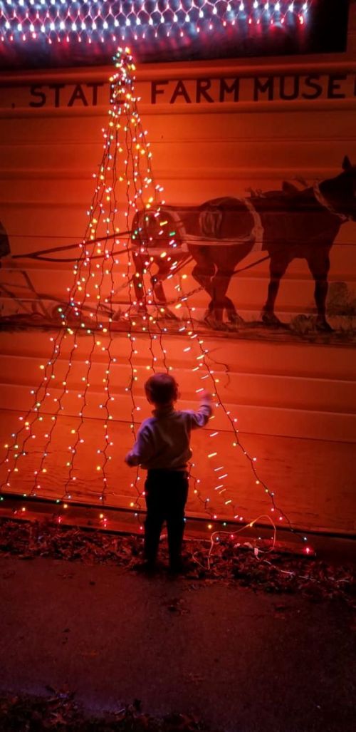 A child decorates a wall with colorful lights shaped like a Christmas tree, illuminated against a dark background.