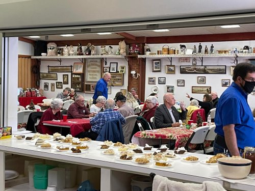 A lively gathering in a dining area with people enjoying food and conversation, surrounded by decorative items on the walls.