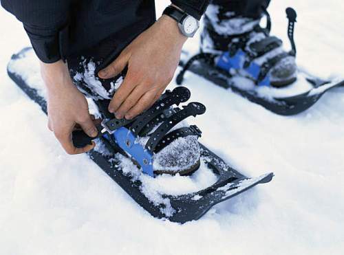 A person fastening snowshoes on their boots while standing in fresh snow.