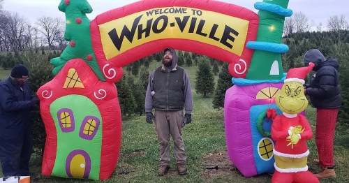 A colorful inflatable archway reading "Welcome to Who-ville" with a man and two others near Christmas trees.