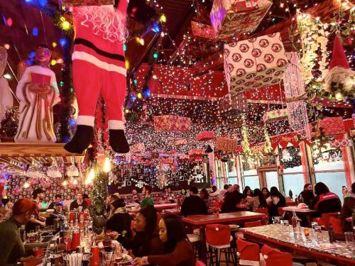 A festive restaurant decorated with colorful lights, holiday ornaments, and Santa figures, filled with diners enjoying their meals.
