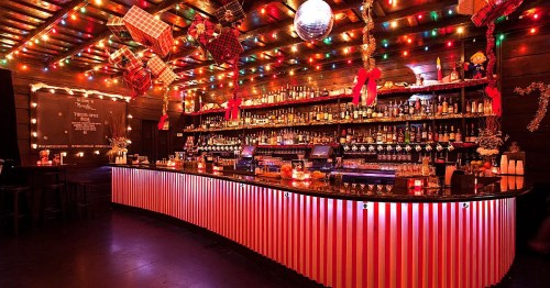 A festive bar decorated with colorful lights, holiday ornaments, and a striped counter, creating a cheerful atmosphere.