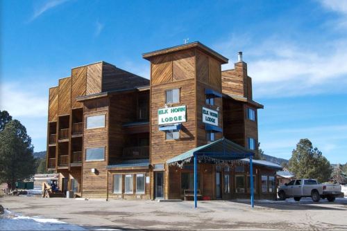 A wooden lodge with multiple levels, featuring a sign that reads "Elk Horn Lodge," set against a clear blue sky.