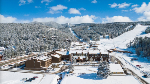 A snowy landscape featuring a resort surrounded by mountains and ski slopes under a clear blue sky.